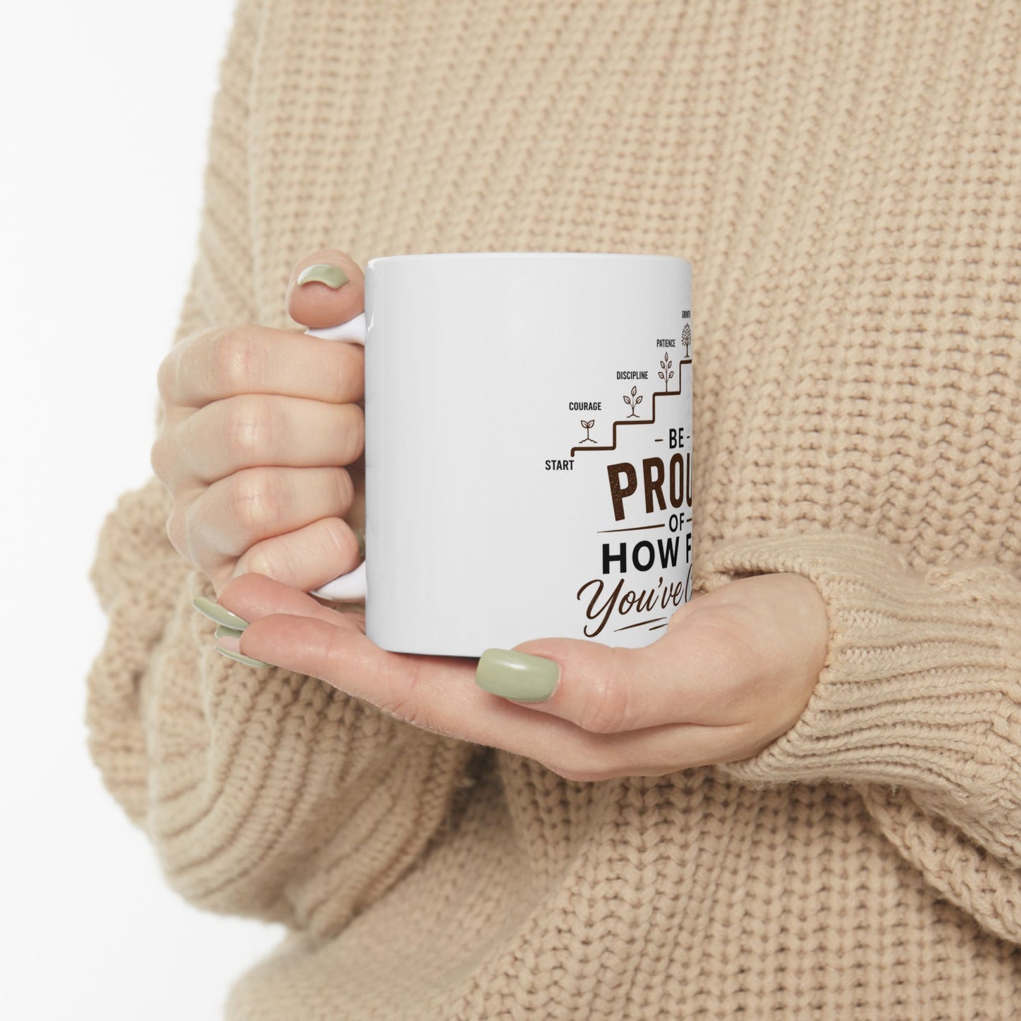 Person holding a white mug with text design, wearing a beige sweater.